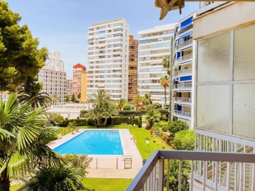Benidorm apartment complex with blue swimming pool, green gardens, palm trees, and modern white buildings with balconies