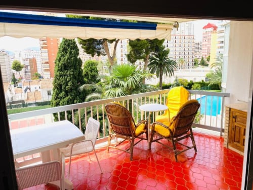 Sunny balcony terrace at Zafiro Apartments in Benidorm with rattan chairs, yellow cushions, and garden city views