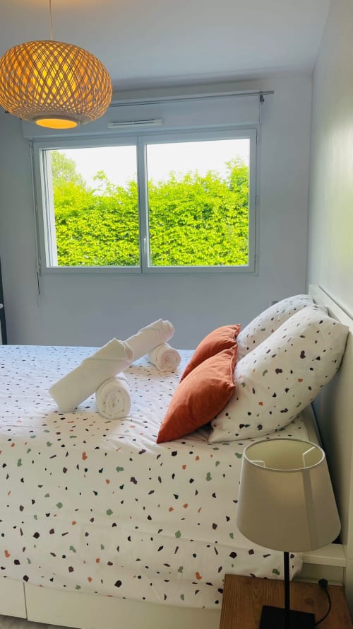 Chambre moderne à la Conciergerie Pour Tous By Patty à Darazac avec lit, linge de maison à motifs, luminaire suspendu tressé et touches vertes