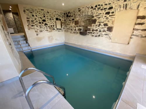 Piscine intérieure du Domaine du Bez à Saint Laurent D'Olt, aux murs de pierre et rampes métalliques