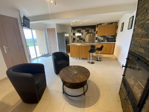 Salon moderne du Domaine du Bez avec fauteuils noirs, table basse en bois, cuisine ouverte et vue sur les montagnes