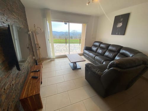 Salon moderne de villa au Domaine du Bez avec canapé en cuir, cheminée et vue sur les montagnes par les portes vitrées