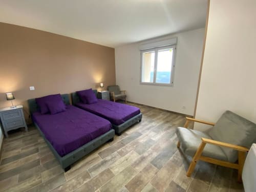 Chambre moderne de la villa Le Domaine du Bez avec lits jumeaux, literie violette, vue sur les montagnes et mobilier contemporain.