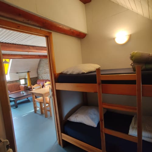 Slaapkamer met stapelbedden in La Ferme De Werpin B&B in Hotton, houten bedframes en open deuropening naar de woonkamer