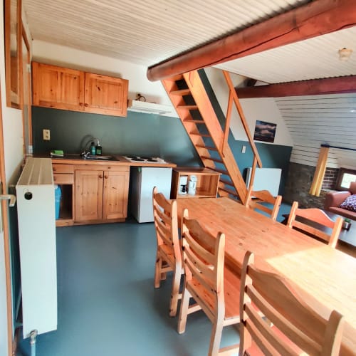 Open keuken en eetkamer in appartement La Ferme De Werpin met houten meubels en zoldertrap