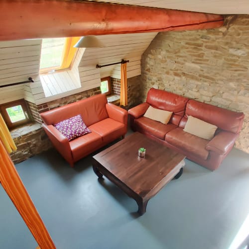 Modern loftzitgedeelte in La Ferme De Werpin met rode lederen banken, houten salontafel en zichtbare bakstenen muren