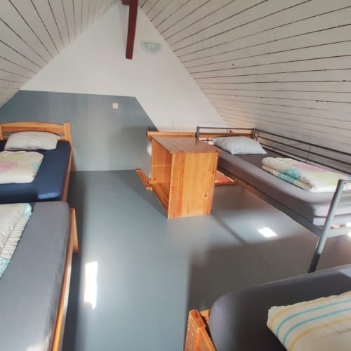 Zolderkamer met vier bedden in La Ferme De Werpin, met houten bedframes en gestreepte beddengoed onder een schuin plafond.