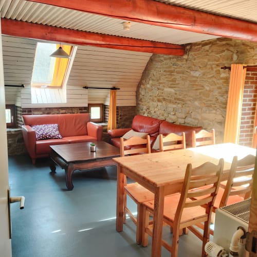 6-persoons appartement La Ferme De Werpin met eettafel, rode bank, stenen muren en tuinuitzicht door dakraam