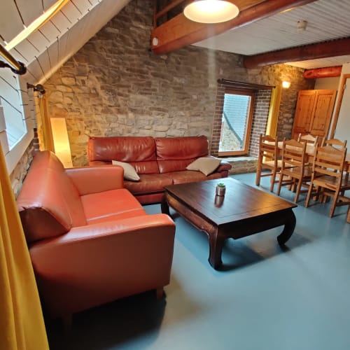 Salon rustique moderne avec sièges en cuir rouge, murs en pierre apparente et poutres en bois à La Ferme De Werpin
