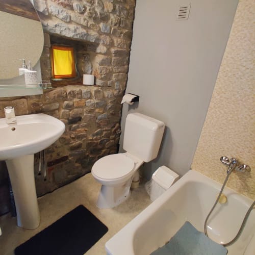 Modern bathroom in La Ferme De Werpin apartment with stone wall, white fixtures, toilet, sink and bathtub in Hotton, Belgium