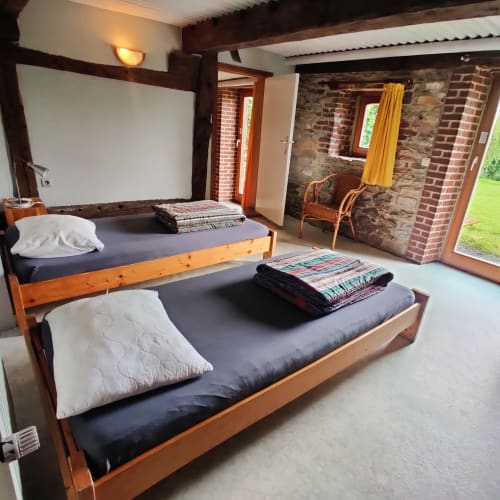 Spacious bedroom at La Ferme De Werpin B&B in Hotton with two wooden beds, white pillows, dark bedding, exposed brick walls,