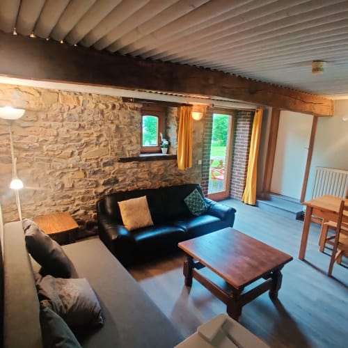 Spacious ground floor apartment living area at La Ferme De Werpin, Hotton with stone walls, black sofa, wooden table and
