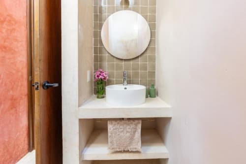 Moderno lavamanos de Casa Tuch B&B en Mérida con espejo redondo, lavatorio blanco, flores rosas y estantería integrada