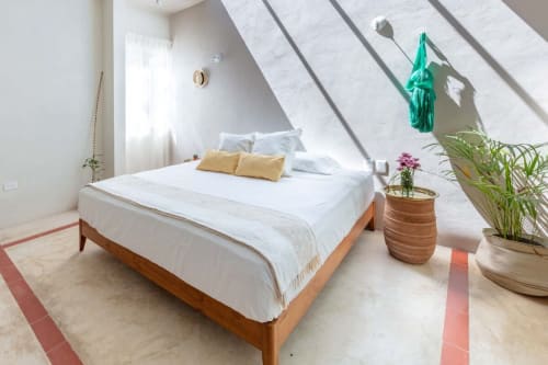 Luminosa recámara de cabaña en Casa Tuch, Mérida, con cama de madera, almohadas amarillas, plantas en macetas y techo inclinado con luz natural