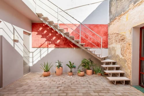 Patio moderno de Casa Tuch Mérida con escaleras geométricas, muro rojo, plantas en macetas y elementos de piedra