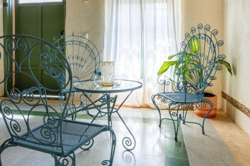 Mobiliario de hierro forjado azul ornamentado en la terraza de Casa Tuch B&B en Mérida, México, con planta en maceta y puertas verdes