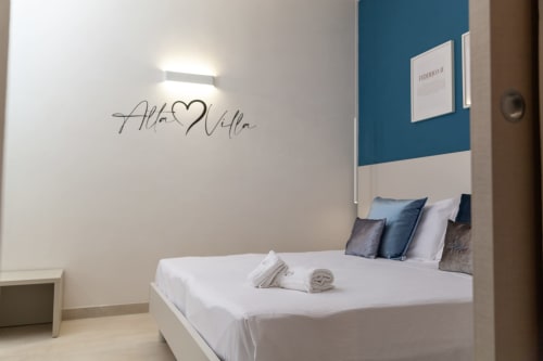 Modern bedroom at Altavilla Boutique Holidays, Marsala featuring queen bed with blue accent wall and decorative script