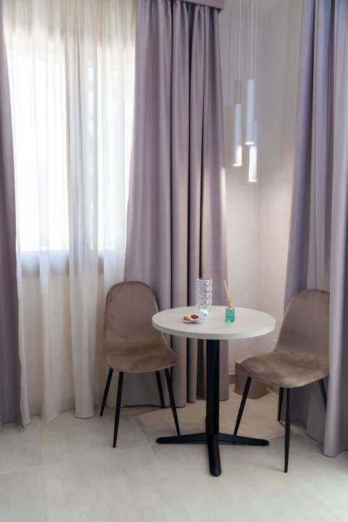 Modern seating area in Altavilla Boutique hotel, Marsala with round white table, velvet chairs, and floor-to-ceiling curtains