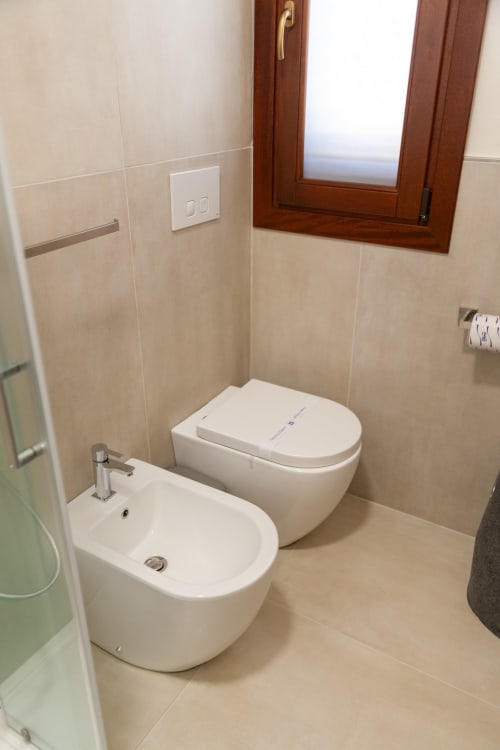 Modern bathroom with white bidet and toilet, beige tile walls, wooden window frame at Altavilla Boutique Holidays House in
