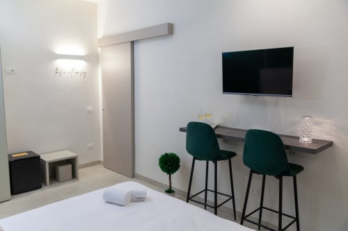 Camera moderna di Altavilla Boutique con letto bianco, smart TV, sedie bar verdi, scrivania e design minimalista