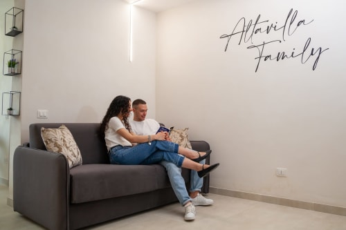 Couple relaxing on gray couch in modern Family Room at Altavilla Boutique Holidays House, Marsala