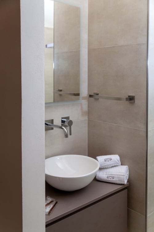 Modern bathroom with white bowl sink, mirror, wall-mounted faucet and folded towels at Altavilla Boutique in Marsala