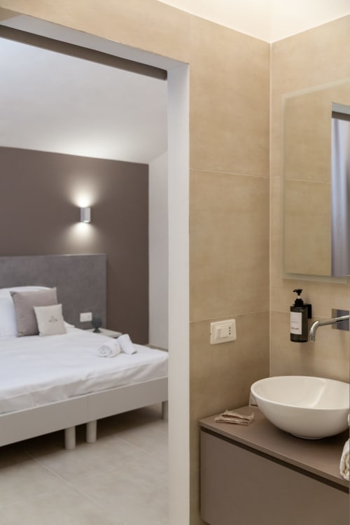 Modern bathroom with white vessel sink connected to beige bedroom in Marsala boutique hotel Family Room