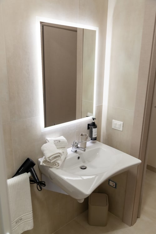 Modern bathroom sink with illuminated mirror, white towels, and amenities at Altavilla Boutique Holidays House in Marsala