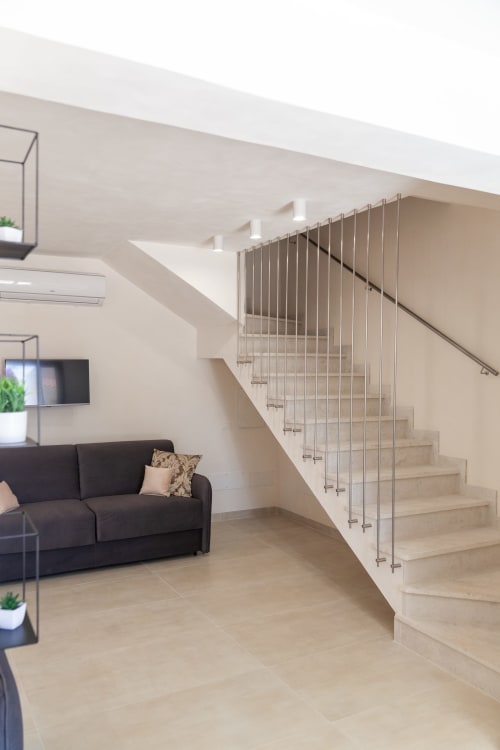 Modern living room with black sofa, wooden staircase with metal railings at Altavilla Boutique Holidays in Marsala