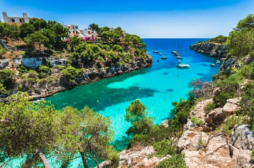 Cala turquesa con embarcaciones, villas blancas y pinos en Colonia de Sant Jordi