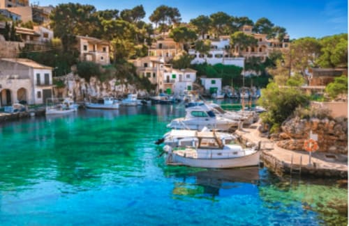 Cala turquesa del Mediterráneo con barcas de pesca y villas de colores pastel en Colonia de Sant Jordi, España