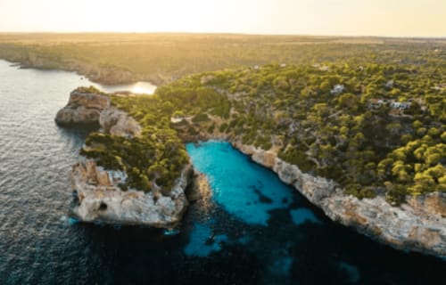 Vista aérea de cala turquesa con acantilados de piedra caliza blanca y bosques de pinos en Colonia de Sant Jordi