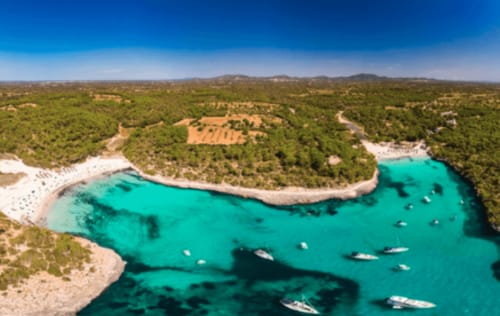 Cala turquesa en Colonia de Sant Jordi con embarcaciones, playa blanca, pinar y montañas
