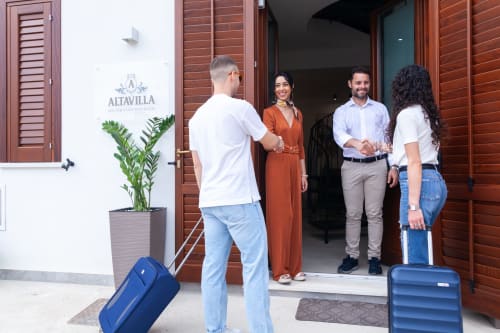 Guests arriving at Altavilla Boutique Holidays House in Marsala with luggage, greeted by staff at entrance