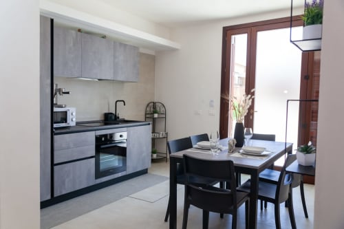 Cucina moderna e zona pranzo presso Altavilla Boutique Holidays House a Marsala con mobili grigi, tavolo da pranzo nero e