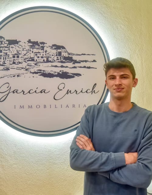 Young man standing in front of Garcia Enrich Immobiliaria office sign in Palafrugell
