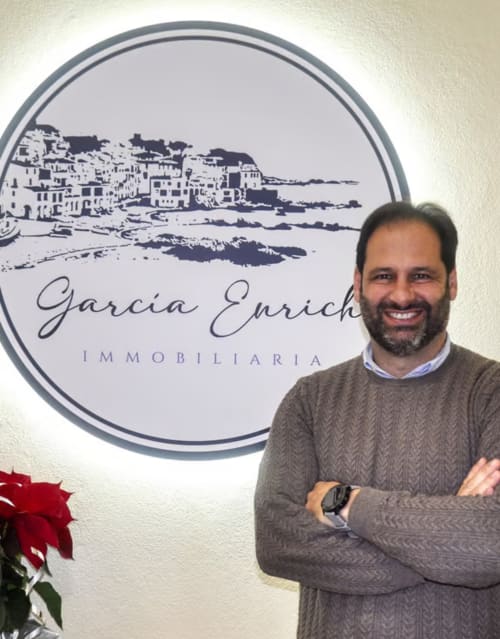 Property manager at Finques Garcia Enrich in Palafrugell, smiling with arms crossed before coastal logo