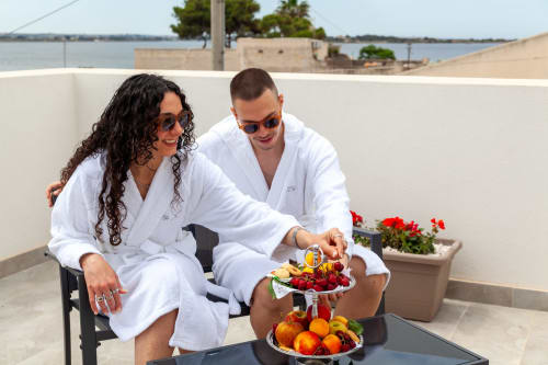 Coppia in accappatoi bianchi gusta frutta sulla terrazza con vista su Marsala, Italia presso Altavilla Boutique Holidays House