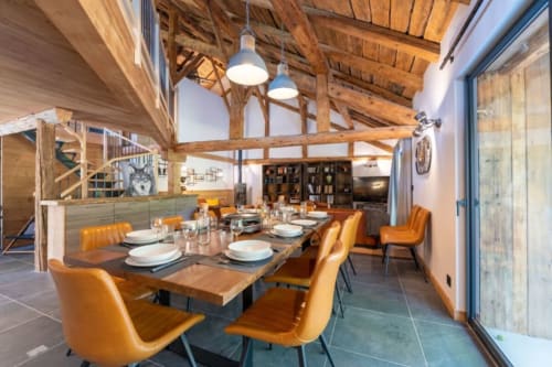 Salle à manger contemporaine du Domaine de l'Epigny avec poutres en bois, chaises oranges et larges baies vitrées sur les Alpes.