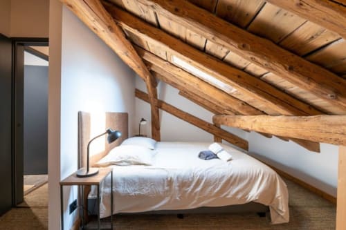 Chambre rustique sous les toits du Domaine de l'Epigny avec poutres apparentes, literie blanche et lampe de bureau noire