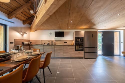 Cuisine ouverte et salle à manger moderne au Domaine de l'Epigny avec poutres en bois, chaises en terre cuite et acier inoxydable
