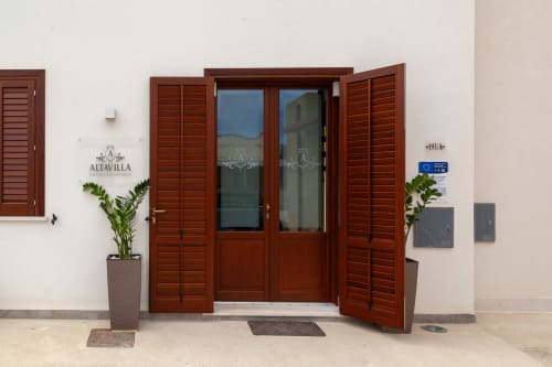 Ingresso della Boutique Altavilla a Marsala con porte in legno rosso, persiane, piante in vaso e facciata accogliente