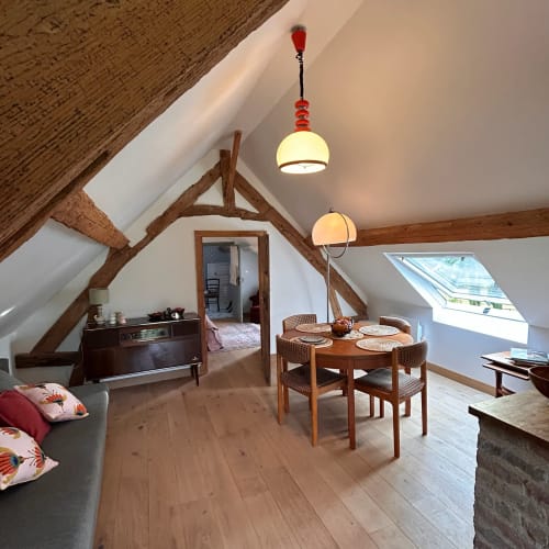 Suite mansardée du Domaine de Blanvatel avec poutres apparentes, table à manger et luminaires suspendus
