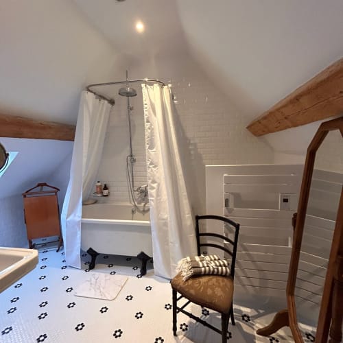 Salle de bain rustique à Domaine de Blanvatel avec poutres apparentes, douche à l'italienne, carrelage noir motifs et chaise vintage.