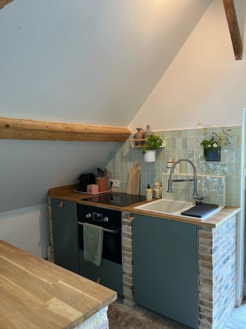 Kitchenette moderne du Domaine de Blanvatel avec mobilier vert, poutres bois et dosseret carrelage sauge