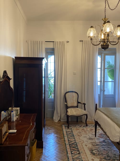 Quarto elegante na Patio Da Villa com móveis de época, cortinas creme, lustre e portas com vista para o jardim