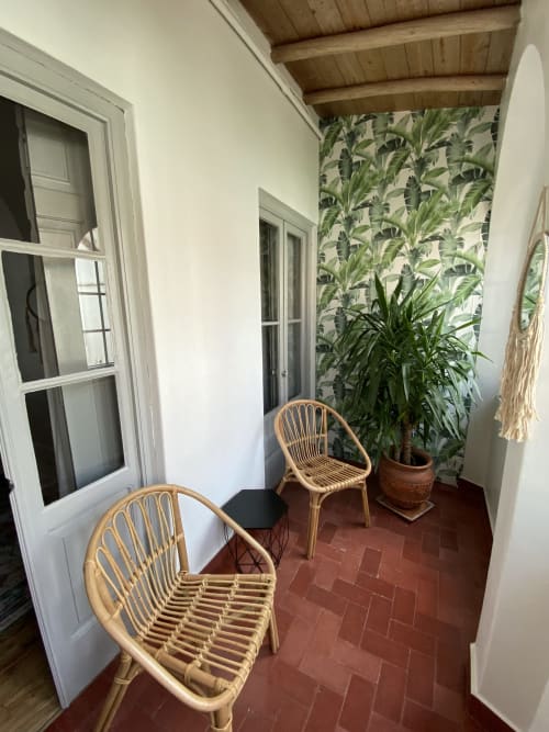 Aconchegante área de estar na varanda do Patio Da Villa com cadeiras de vime, planta em vaso e painel tropical