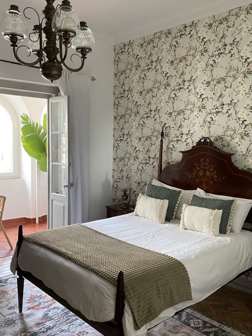 Quarto elegante no Patio Da Villa com cama de madeira ornamentada, papel de parede floral, lustre decorativo e varanda com vista para o jardim