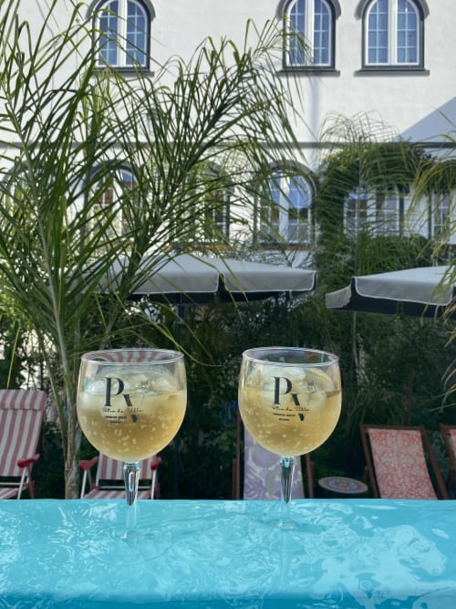 Dois copos de vinho branco à beira da piscina na Patio Da Villa em Coruche, Portugal, com vista para o jardim e espreguiçadeiras listradas