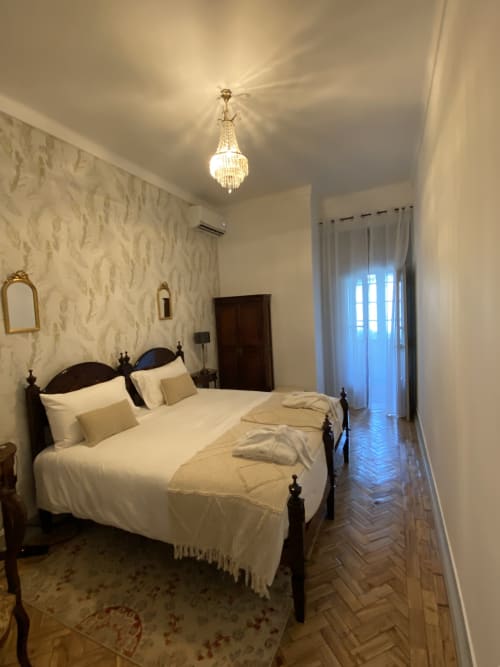 Elegante quarto duplo na Patio Da Villa em Coruche com cama de madeira escura, roupa branca creme, papel de parede estampado, lustre e